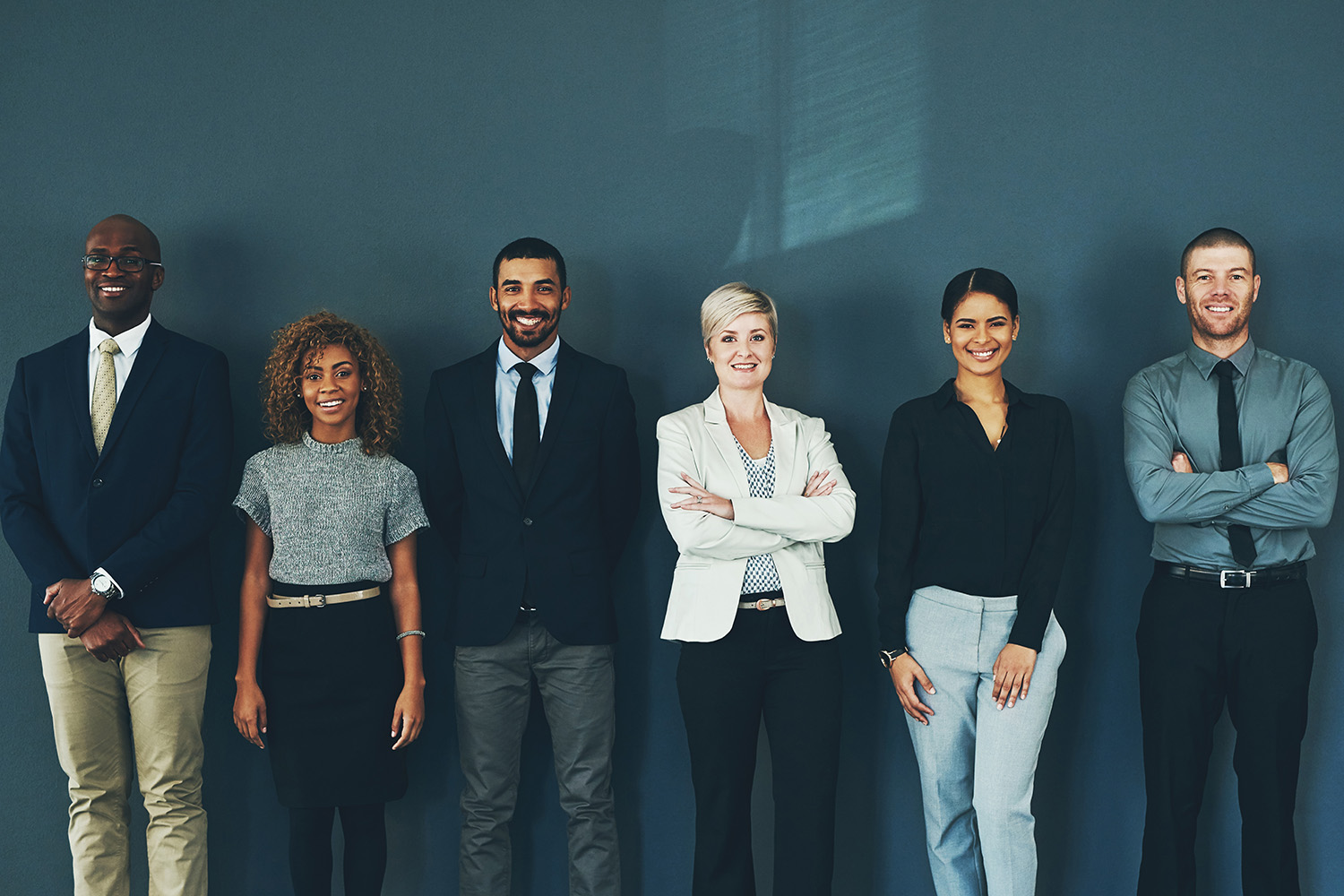 Group of diverse business people smiling and standing in front of a blue wall.